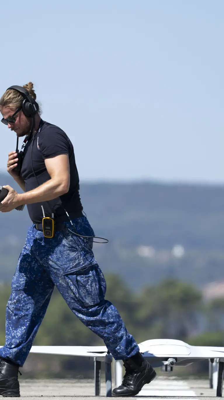 Een marinecollega loopt langs een drone die op de startbaan staat.