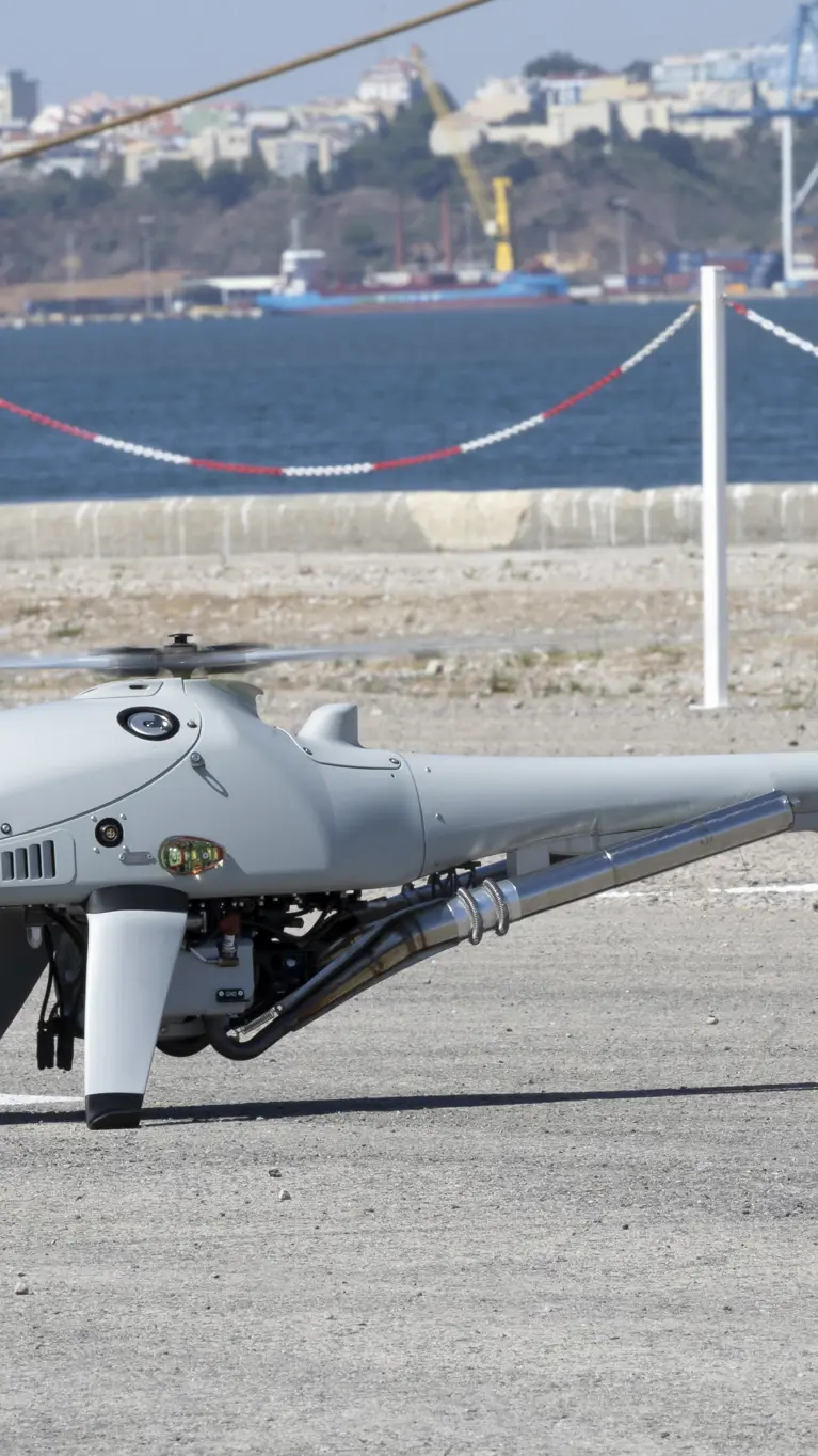 Een drone staat op het asfalt met op de achtergrond water en huizen.