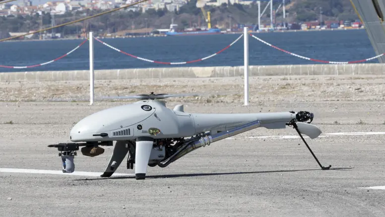 Een drone staat op het asfalt met op de achtergrond water en huizen.