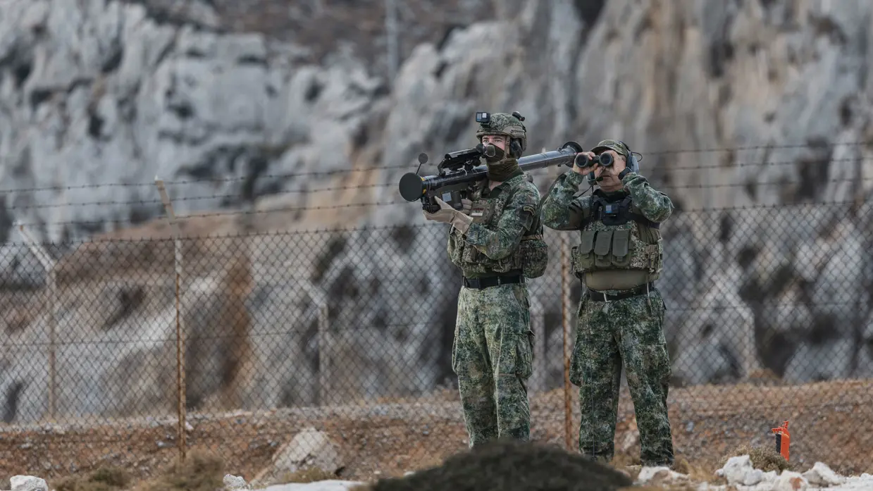  2 militairen staan naast elkaar. De linker heeft het Stinger-wapensysteem op zijn schouder, de rechter kijkt door een verrekijker. 