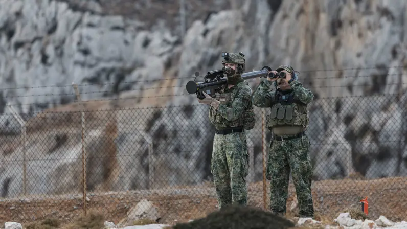  2 militairen staan naast elkaar. De linker heeft het Stinger-wapensysteem op zijn schouder, de rechter kijkt door een verrekijker. 