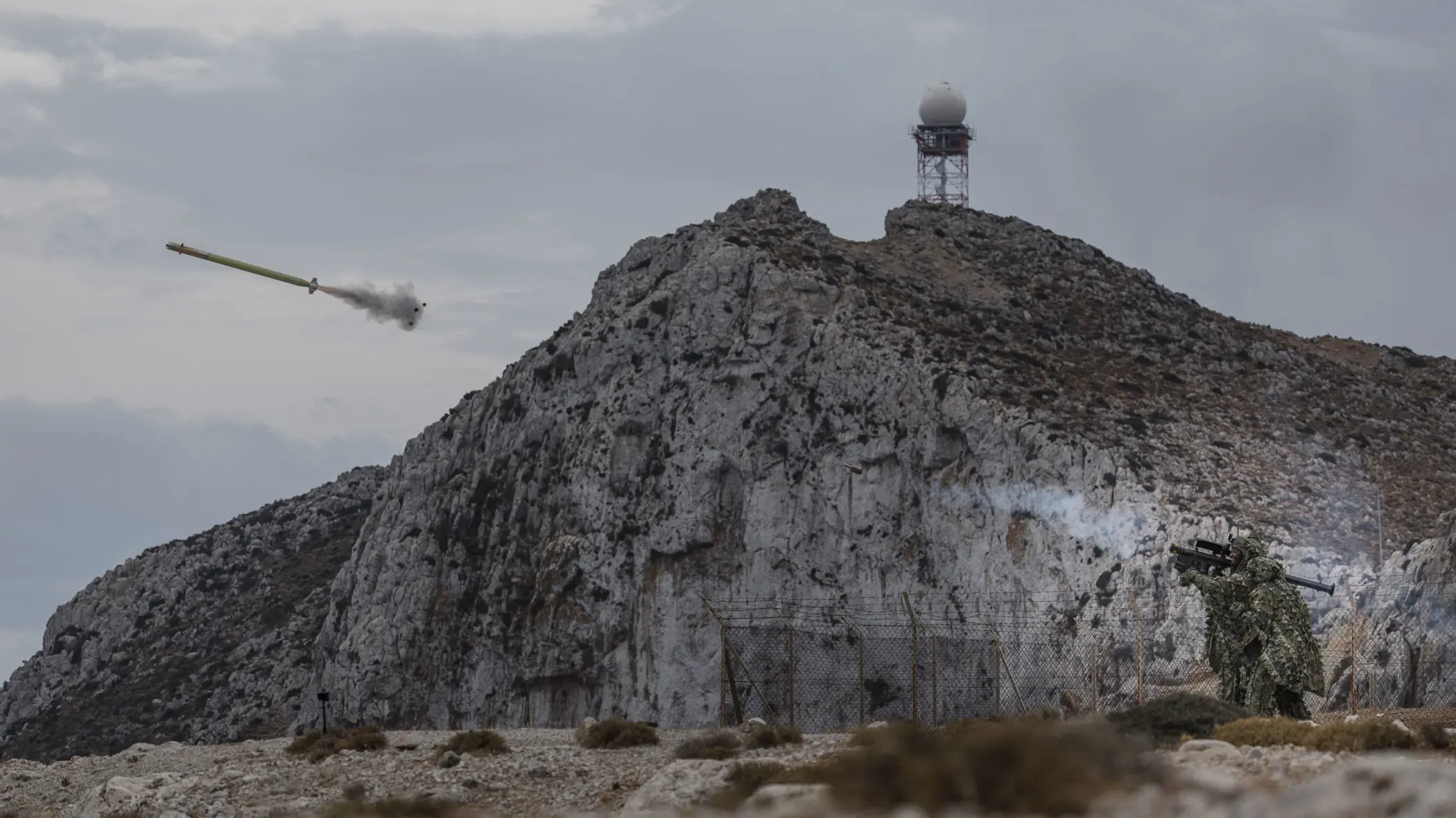 Militairen in een zogeheten ghillie suit (bijzonder soort camouflagepak) schieten een Stinger-luchtdoelraket in een landschap vol rotsen.
