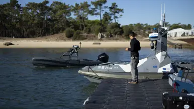 Een man bestuurt een zwart, onbemand bootje vanaf de kade.