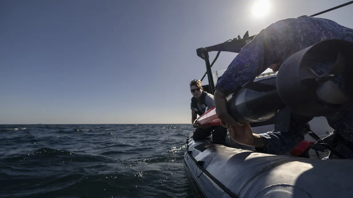 Een vrouw en een man in uniform laten een oranjekleurige torpedo te water vanaf de RHIB. 