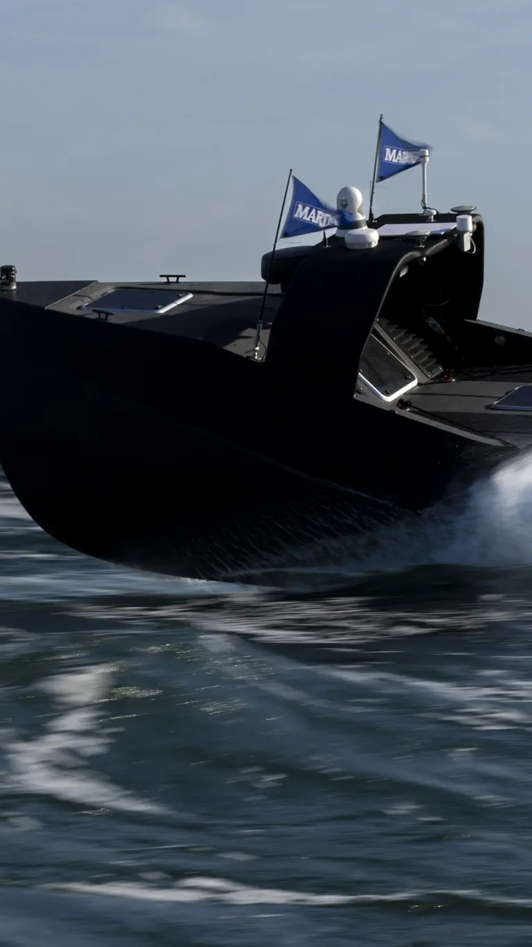 Een zwart, onbemand bootje scheurt over het water en laat daarbij golven achter.