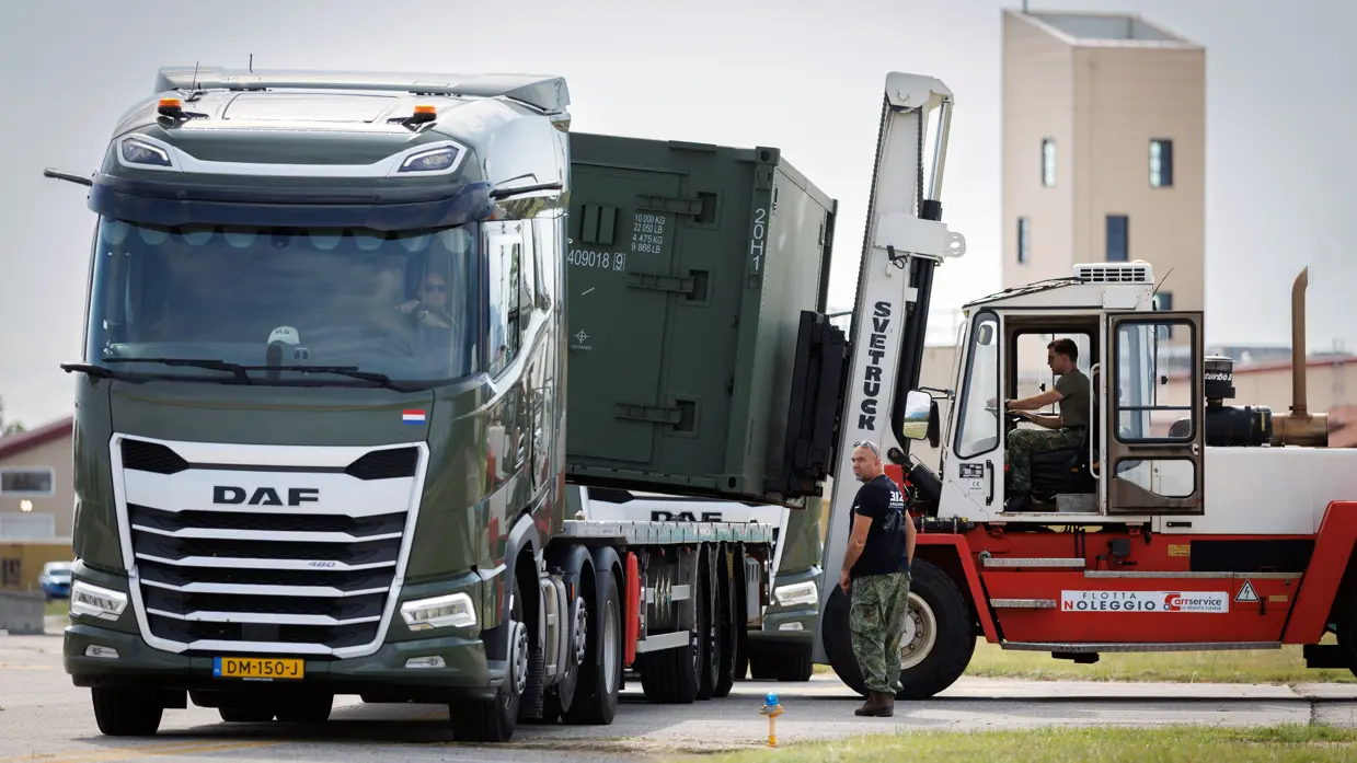 Heftruck tilt container van vrachtwagen. Een militair staat ernaast.