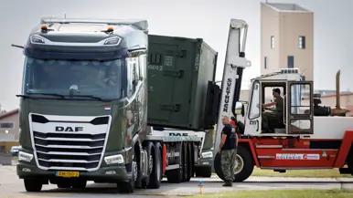 Heftruck tilt container van vrachtwagen. Een militair staat ernaast.