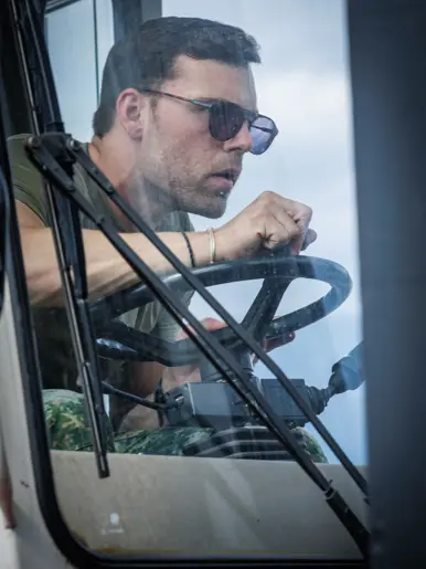 Close-up van militair-chauffeur die geconcentreerd door zijn zonnebril over zijn stuur door de voorruit kijkt.