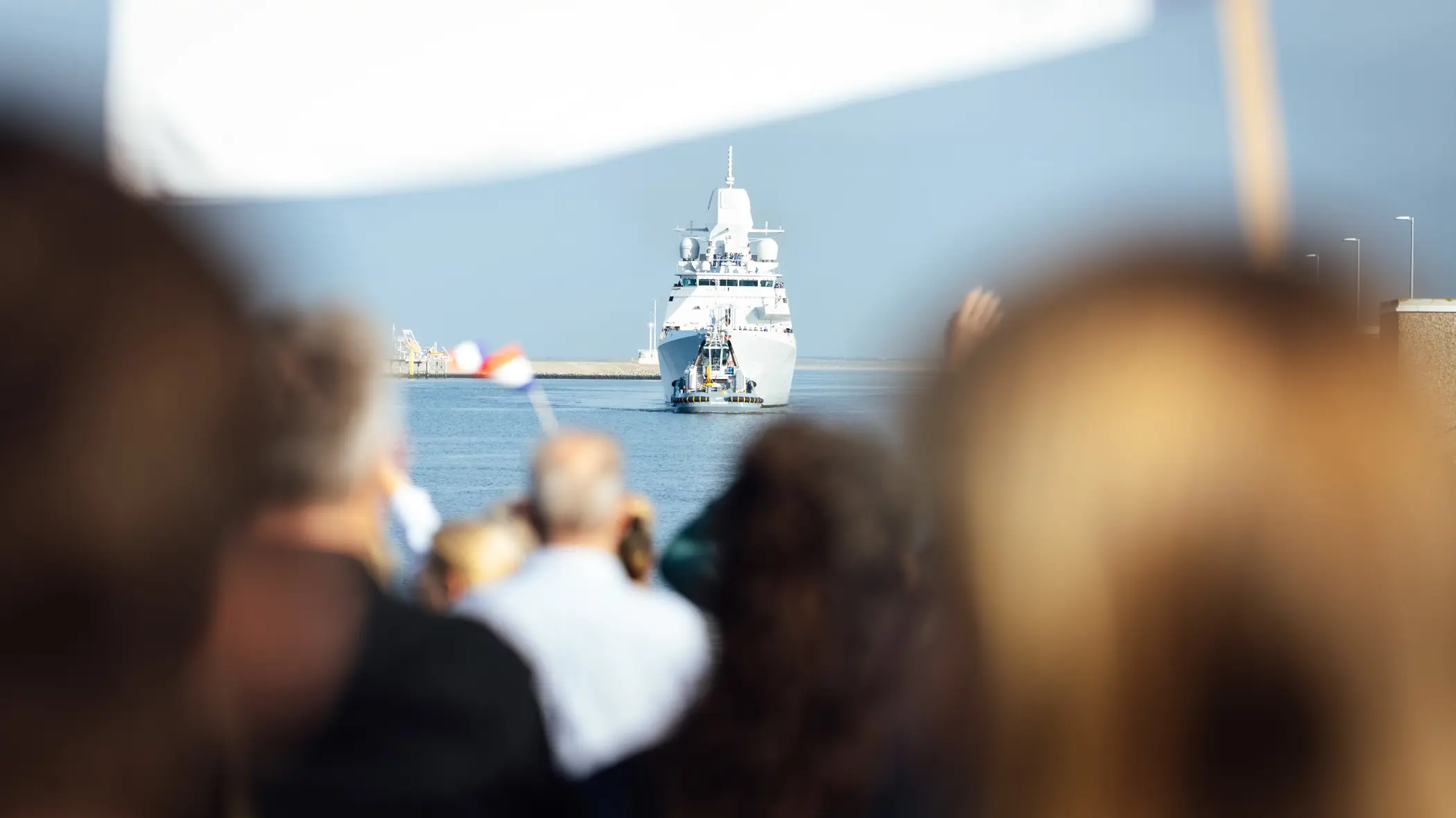  Een marineschip komt aan in de haven terwijl familie aan de kade staat te wachten.