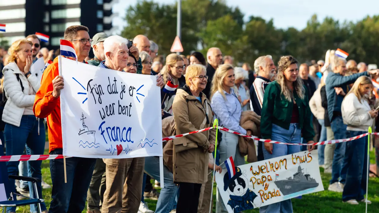 Een grote groep mensen staat aan de kade, enkele van hen houden een spandoek vast. Een groep mensen wandelt over de kade, enkele van hen houden een spandoek vast.