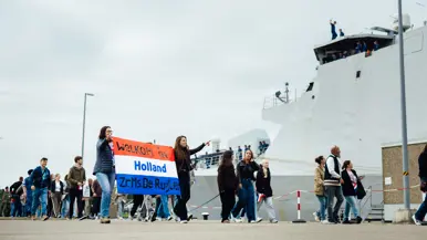 Een groep mensen wandelt over de kade, enkele van hen houden een spandoek vast. 