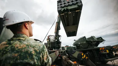 Een militair met witte helm op kijkt hoe een kraanmachinist een serie raketten hijst.