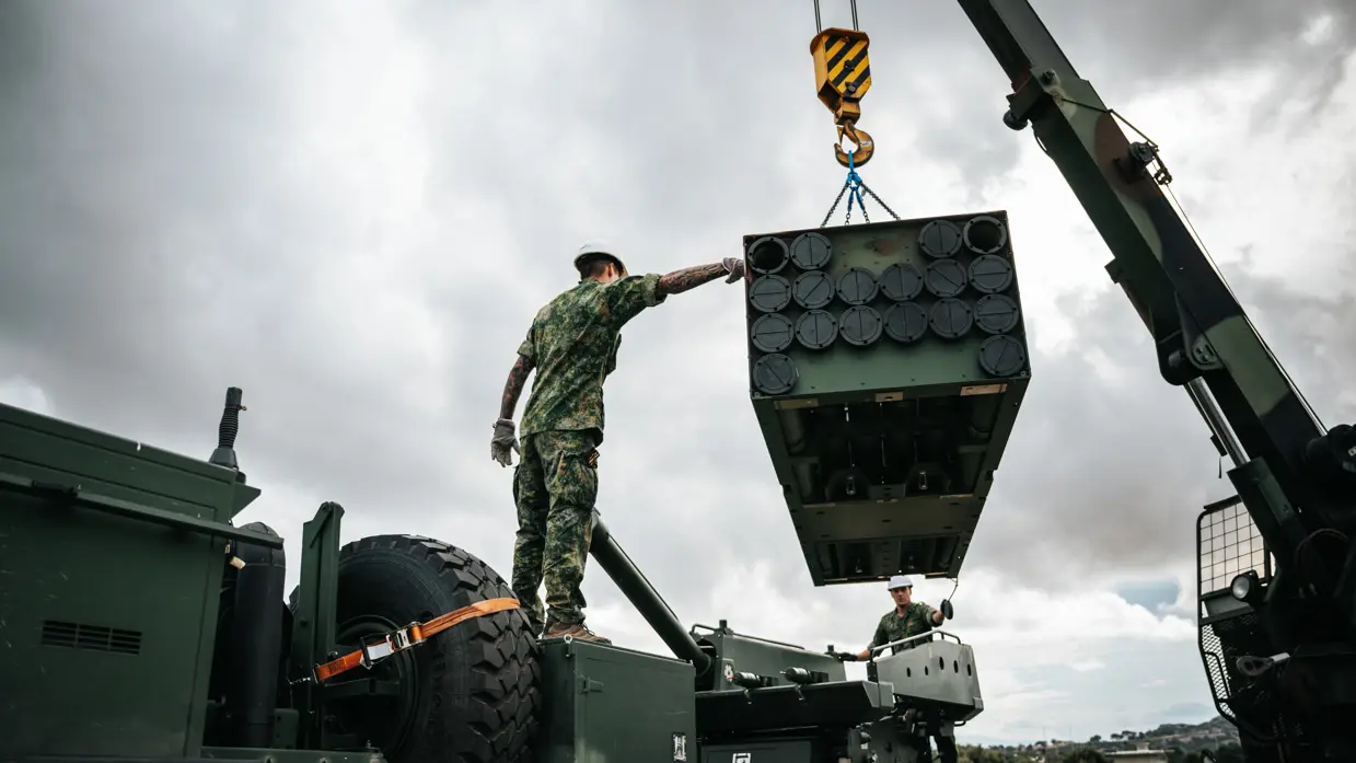 Een militair hijst een onderdeel van de rakettenwerper op het wapensysteem met een hijskraan.
