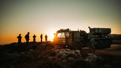 Militairen vormen silhouetten tegen de opkomende zon, terwijl ze bezig zijn met de positionering van de PULS.