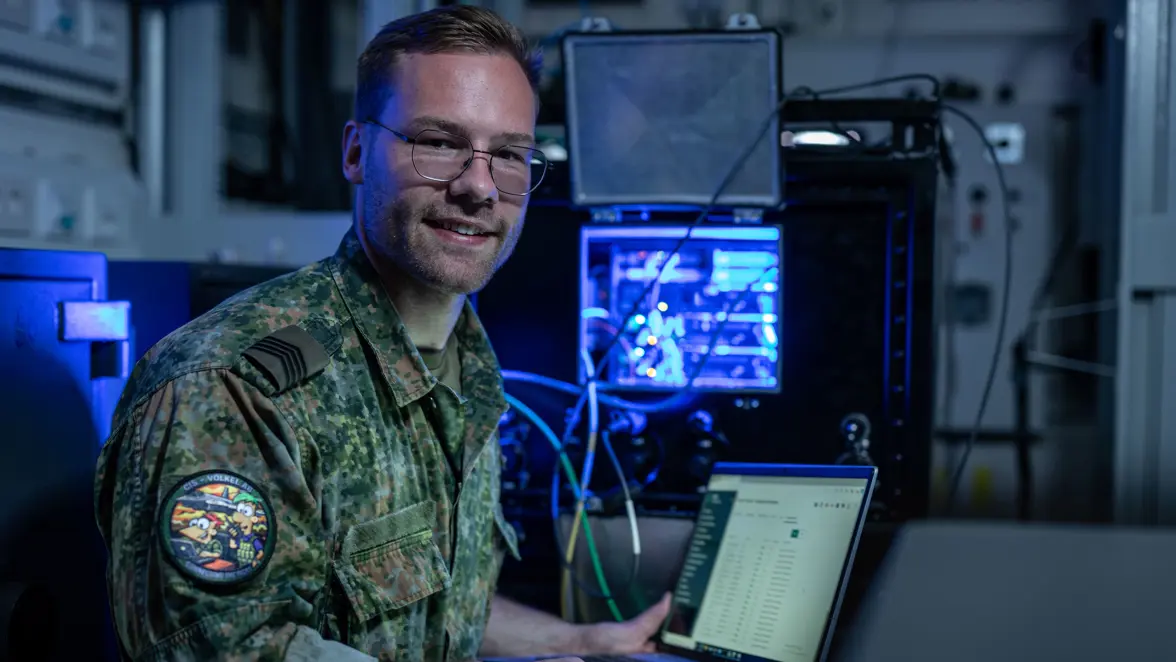 Sergeant-majoor Frank met een laptop in zijn hand. Op een achtergrond een blauw verlichte kast met kabels.