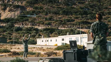 Een militair houdt zijn handen in de lucht, daarboven vliegt een drone.