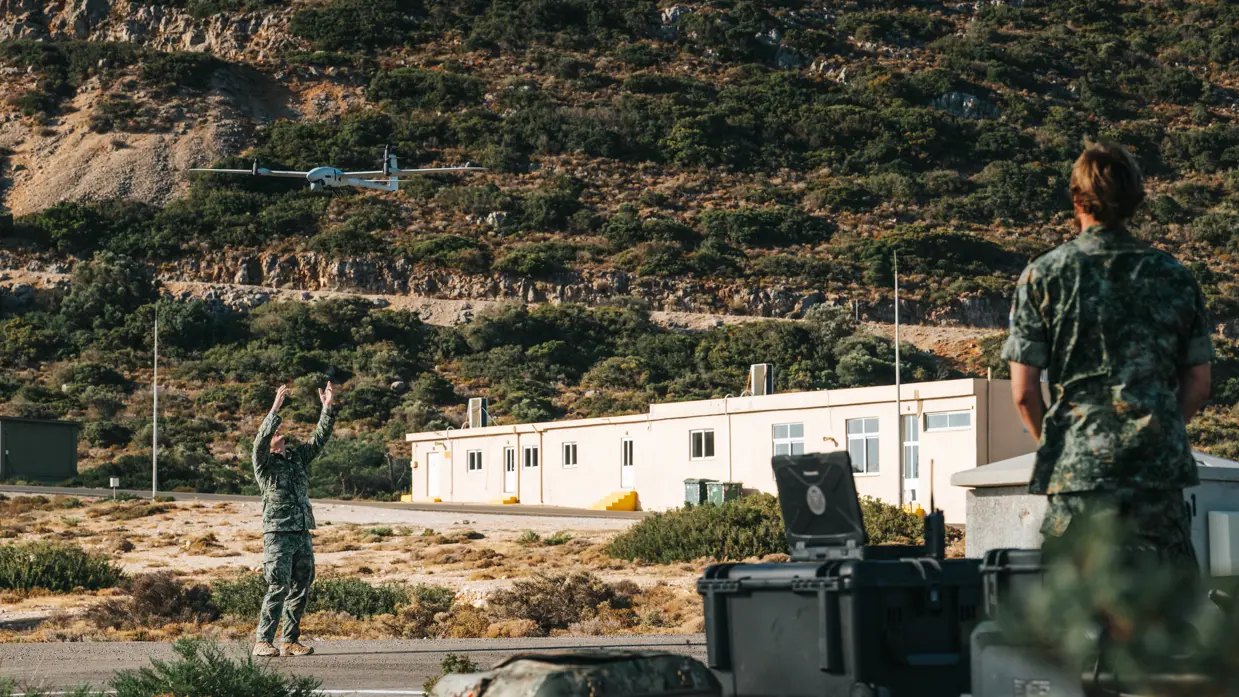 Een militair houdt zijn handen in de lucht, daarboven vliegt een drone.