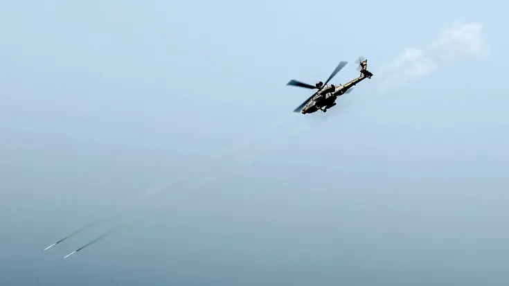 Een Apache duikt naar beneden en vuurt twee raketten af.