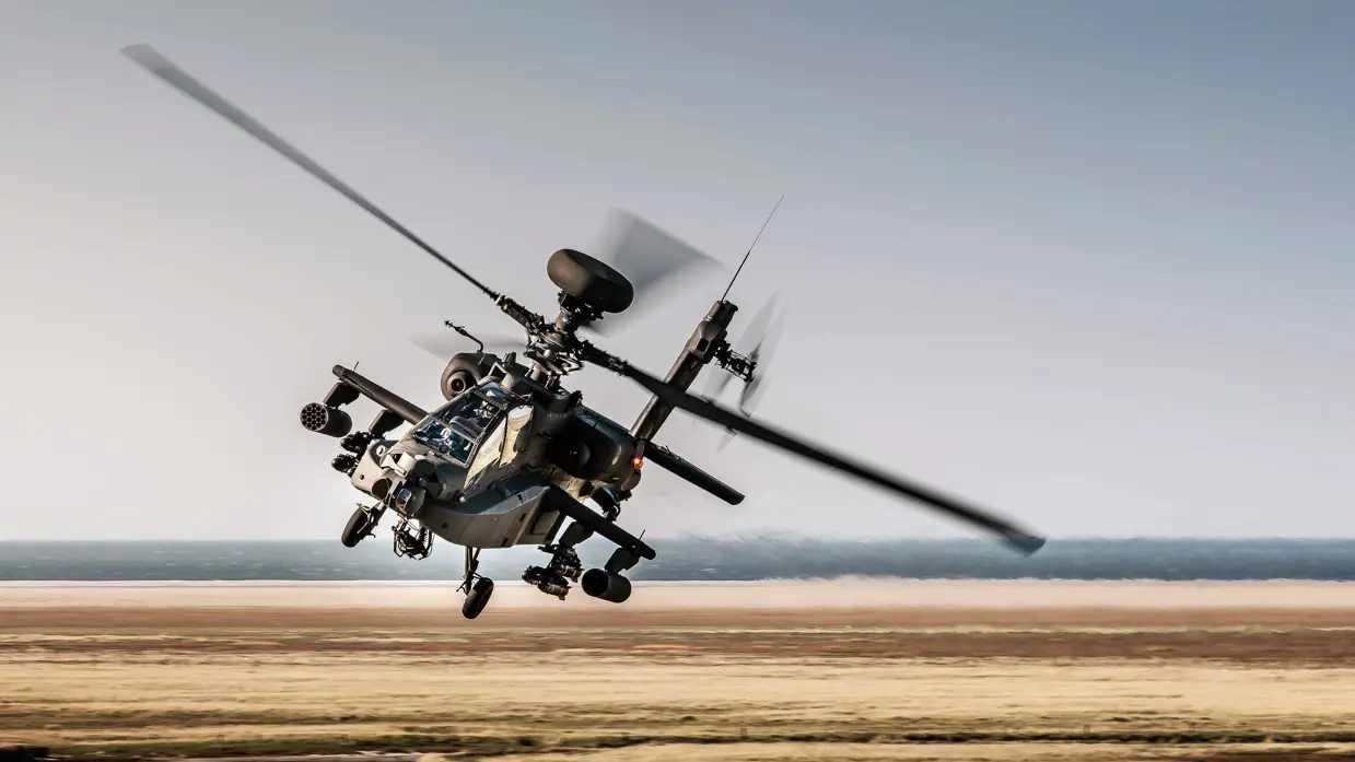 Een Apache maakt een bocht laag vliegend over een kaal bruin landschap.
