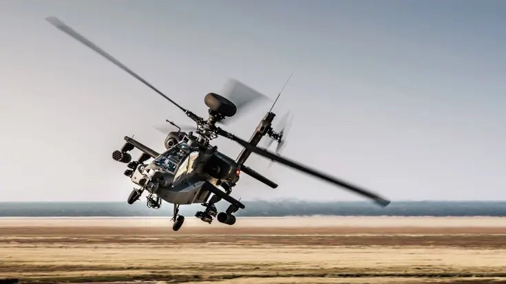Een Apache maakt een bocht laag vliegend over een kaal bruin landschap.