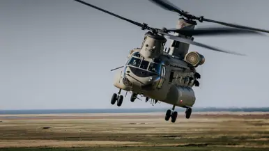 Een grote militaire helikopter in volle vlucht boven een bruin landschap. 