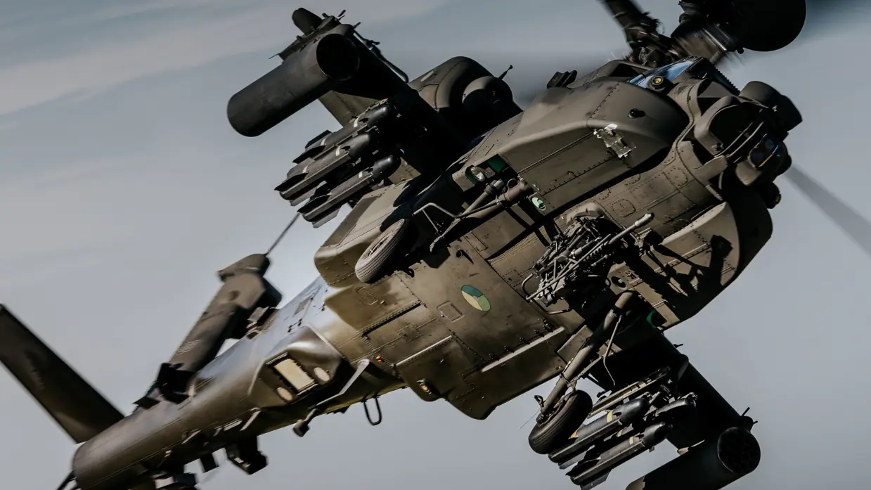 Een zwarte helikopter met bewapening vliegt door de lucht, van de onderkant gezien. 