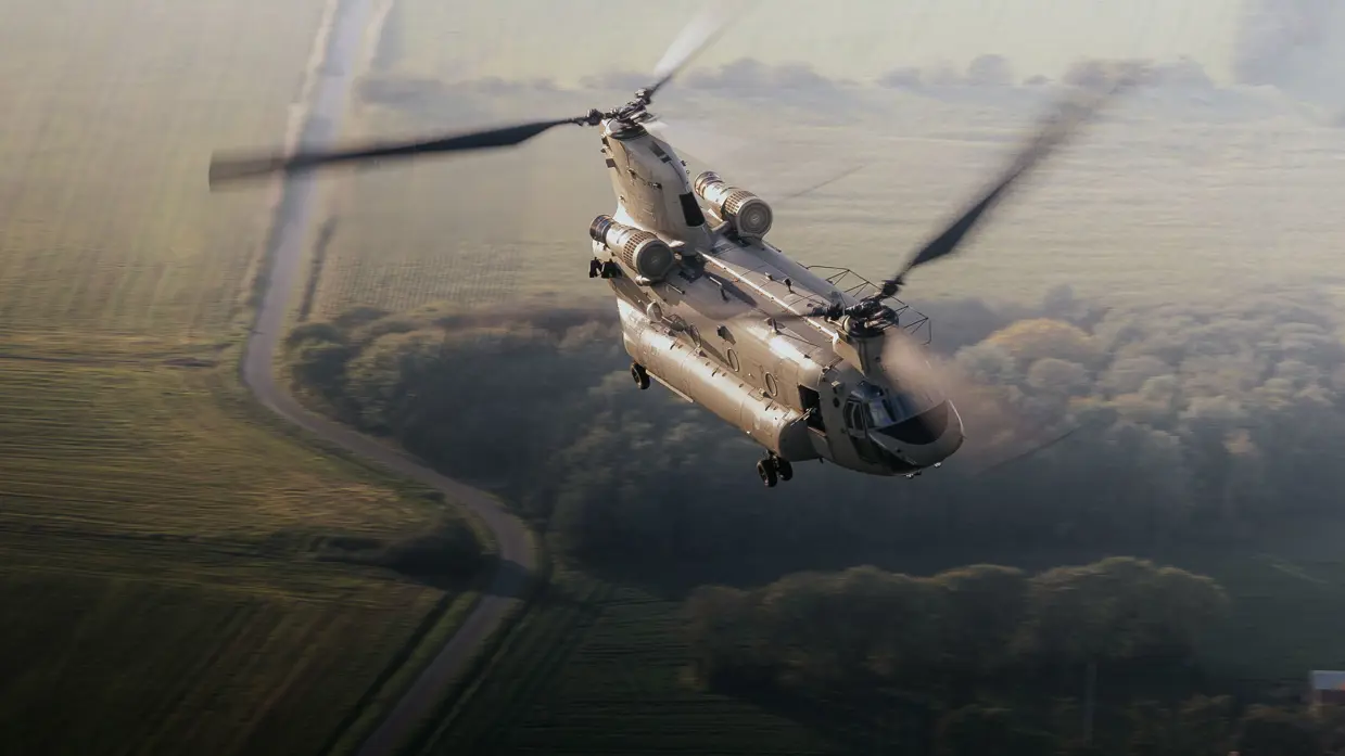 Een grote grijze helikopter vliegt onder een bewolkte lucht.