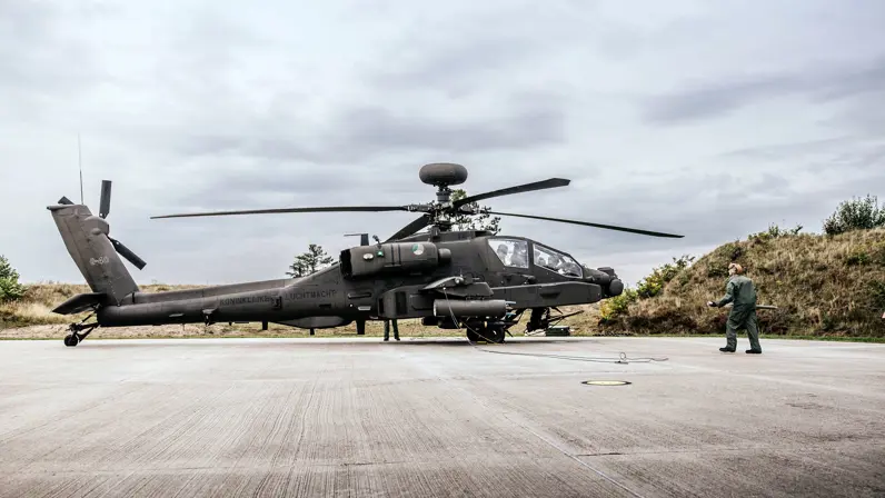 Een militair met een raket in zijn handen loopt naar een Apache.