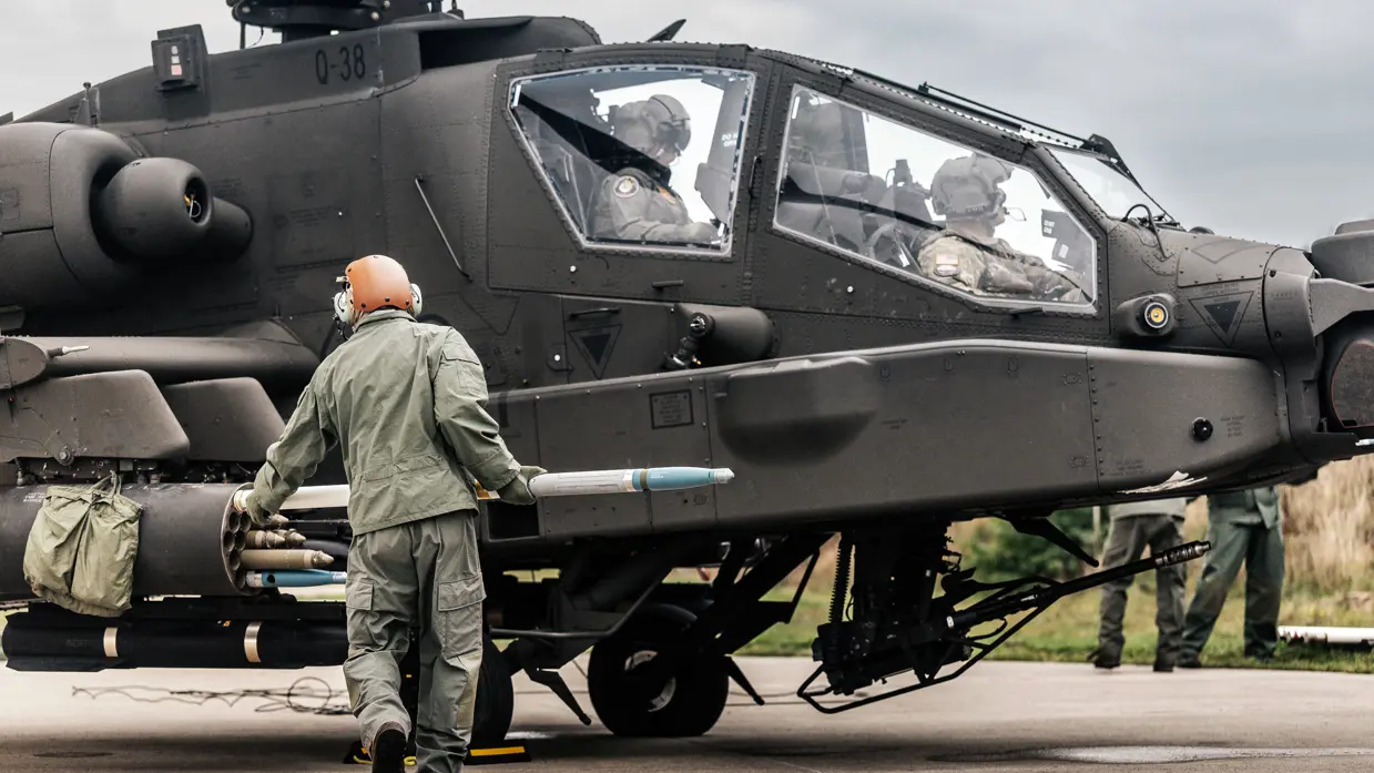 En militair met helm op schuift een raket in een houder aan de zijkant van een Apache.
