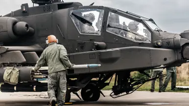 En militair met helm op schuift een raket in een houder aan de zijkant van een Apache.