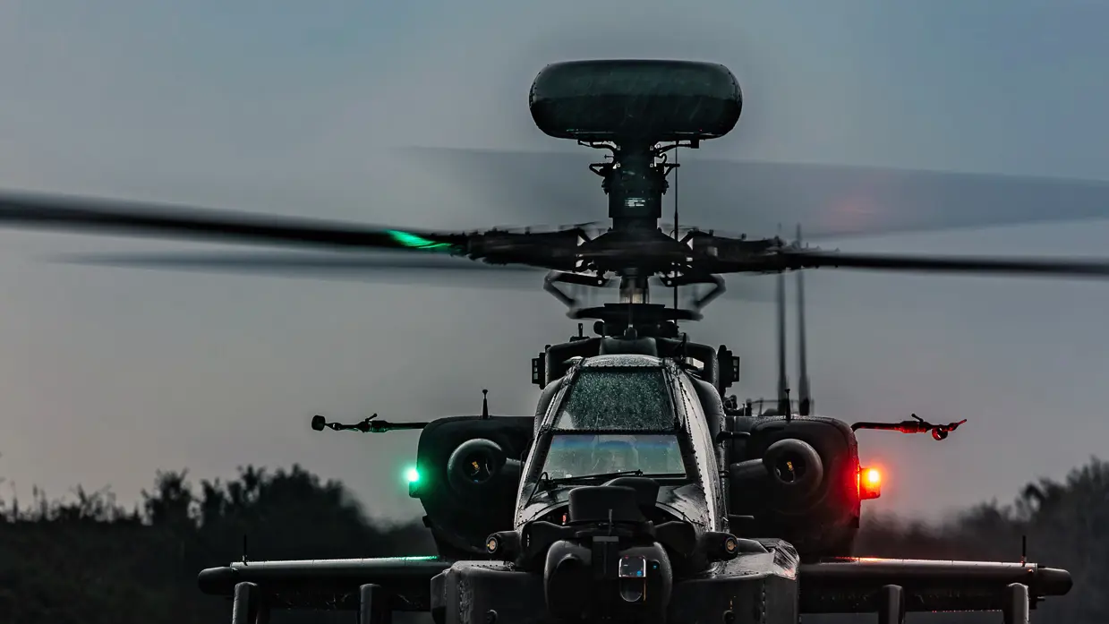  Close up van de voorkant van een Apache die klaarstaat voor vertrek in de schemering. Op de helikopter brandt links een groene en rechts een rode lamp.