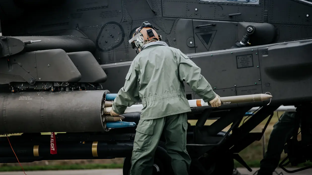 Een militair heeft een lang, cilindervormig object , een raket, in de armen naast een zwarte helikopter.