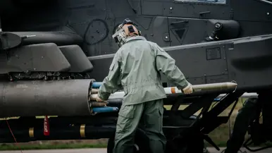 Een militair heeft een lang, cilindervormig object , een raket, in de armen naast een zwarte helikopter.
