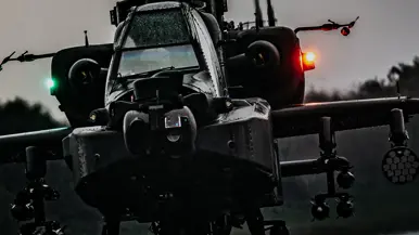 Een donkere helikopter hangt in de schemering boven een landingsbaan. 