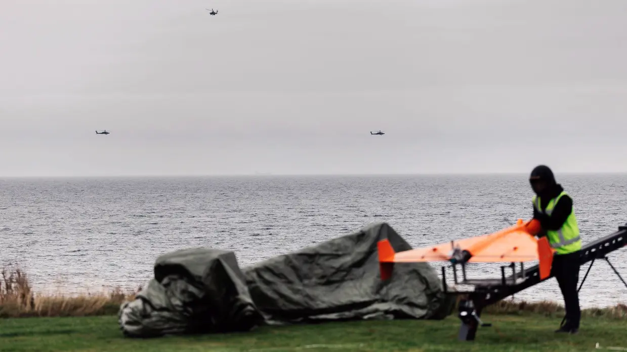 Drie mannen met gele hesjes zetten de oranje drone op een lanceerstelling.