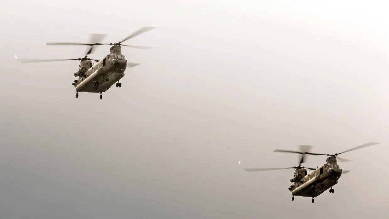Twee Chinooks vliegen onder een grijze lucht.