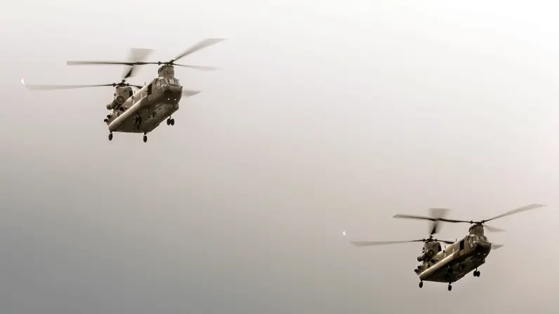 Twee Chinooks vliegen onder een grijze lucht.