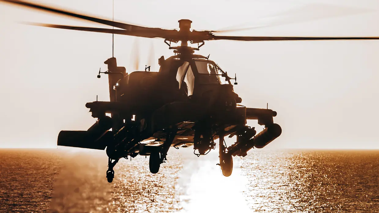  Een zwarte helikopter hang met de ondergaande zon op de achtergrond boven water. 