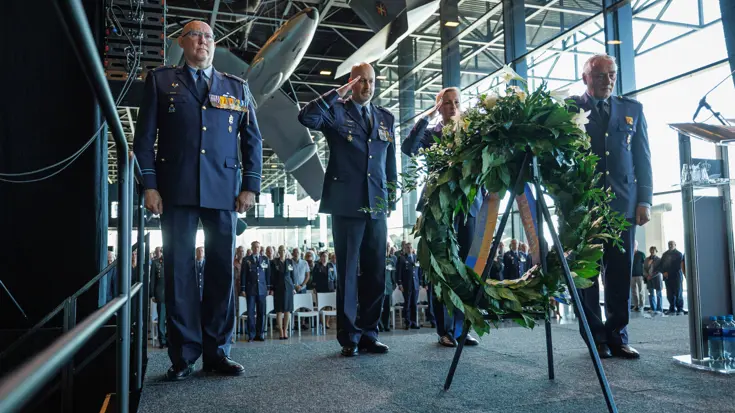 Vier militairen brengen de eregroet terwijl ze naar een grote krans kijken.