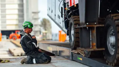 Een geknielde man met groene helm praat door een portofoon.