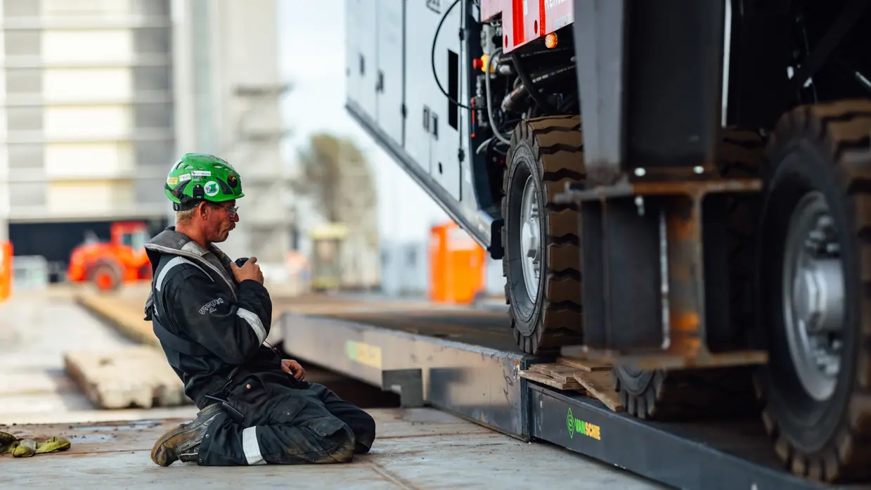 Een geknielde man met groene helm praat door een portofoon.