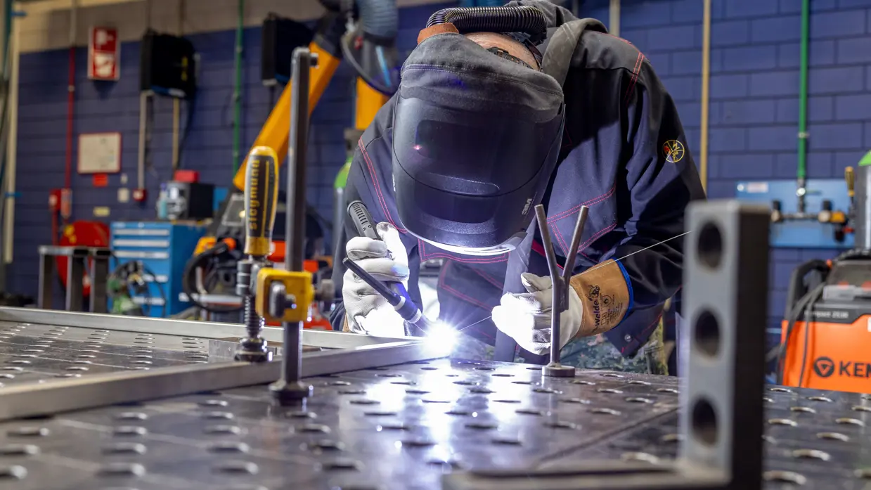 Erik met helm op last een metalen plaat met een heldere lichtflits bij de lasnaad.