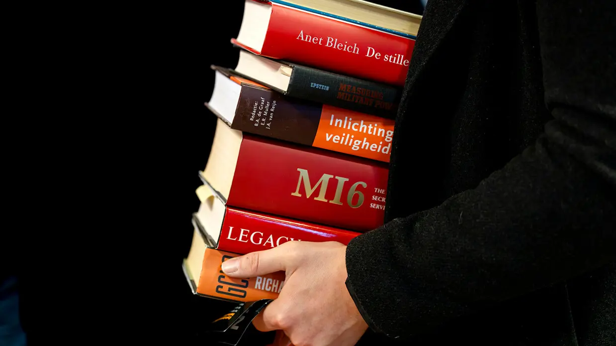 iemand houdt een stapel boeken vast.