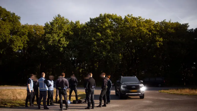 Een groep militairen van de PBB die met voertuigen samenkomt op een geasfalteerde weg in een bosrijke omgeving tijdens een oefening.