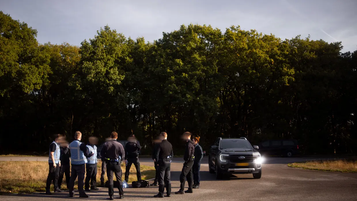 Een groep militairen van de PBB die met voertuigen samenkomt op een geasfalteerde weg in een bosrijke omgeving tijdens een oefening.