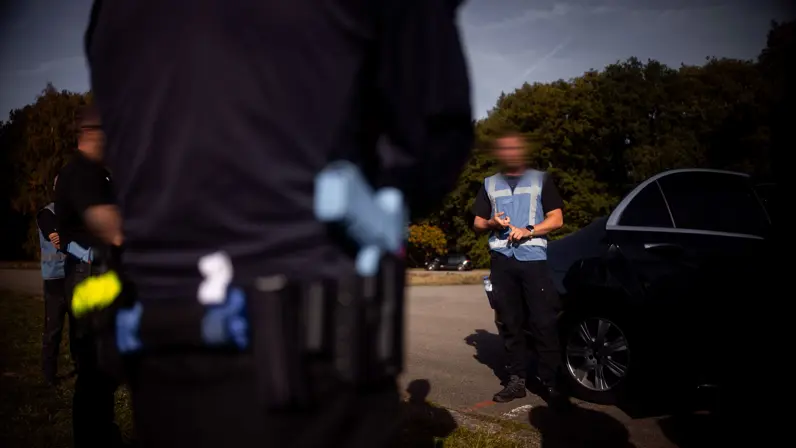Close-up van de uitrusting van een militair van de PBB, met een focus op het holster met een blauw trainingswapen aan de riem.