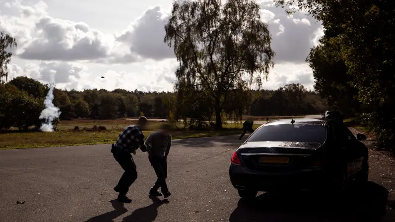 Een militair van de PBB die tijdens een trainingssessie op de Vlasakkers met een trainingswapen dekking geeft bij een donkere personenauto.