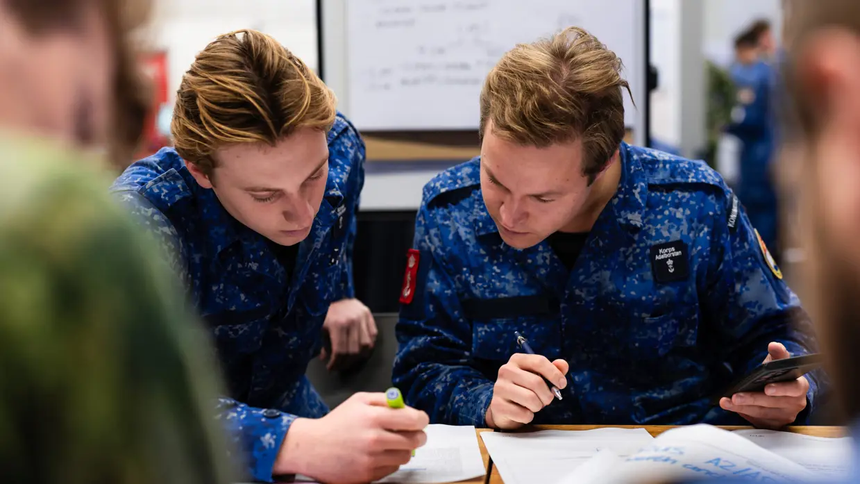 Twee militairen met pen en telefoon in de hand aan tafel