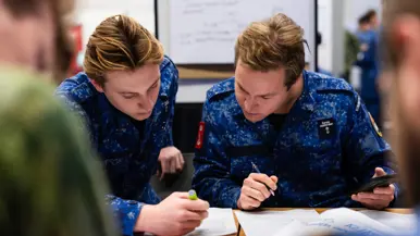 Twee militairen met pen en telefoon in de hand aan tafel