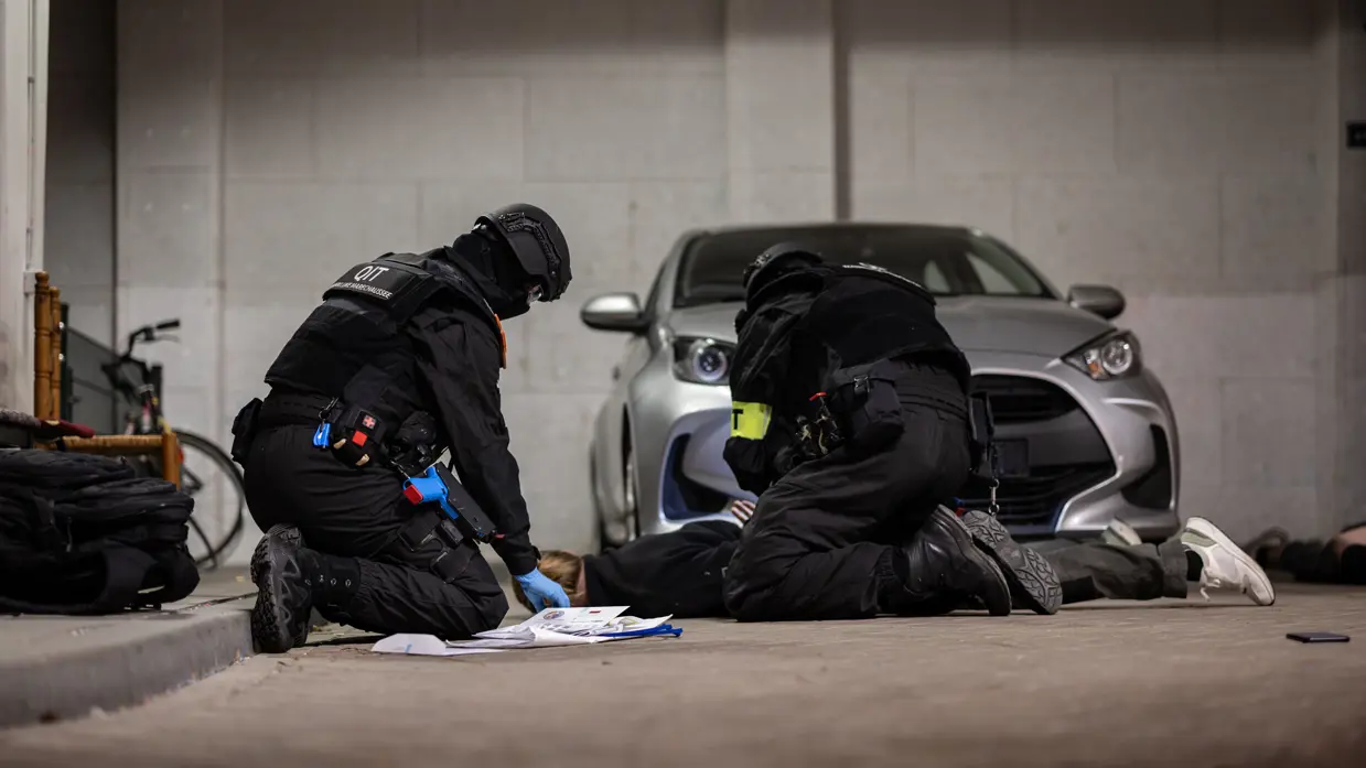Twee marechaussees knielen bij een geboeide verdachte die op de grond ligt.